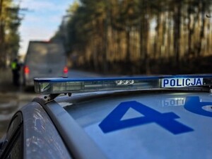 Radiowóz policyjny stojący na poboczu. W tle policjanci kontrolują ciężarówkę.