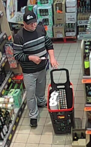 Na zdjęciu mężczyzna w czapce z daszkiem, w swetrze i szarych spodniach podczas zakupów w sklepie.