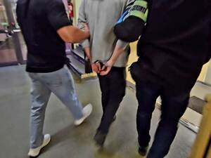 Zatrzymanego mężczyznę w kajdankach prowadzą korytarzem nieumundurowani policjanci.